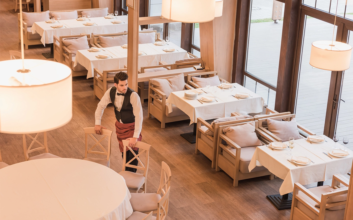 Hero image of a male waiter at a restaurant preparing a table before service.